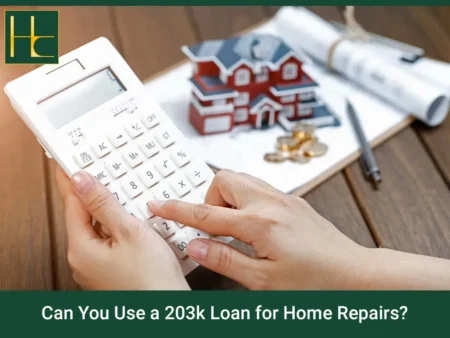 Hands using a calculator beside a model house, coins and blueprints to plan a 203(k) home repair loan