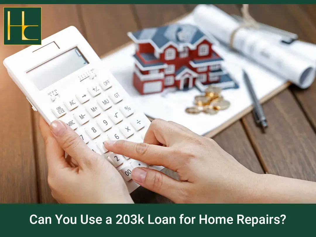 Hands using a calculator beside a model house, coins and blueprints to plan a 203(k) home repair loan